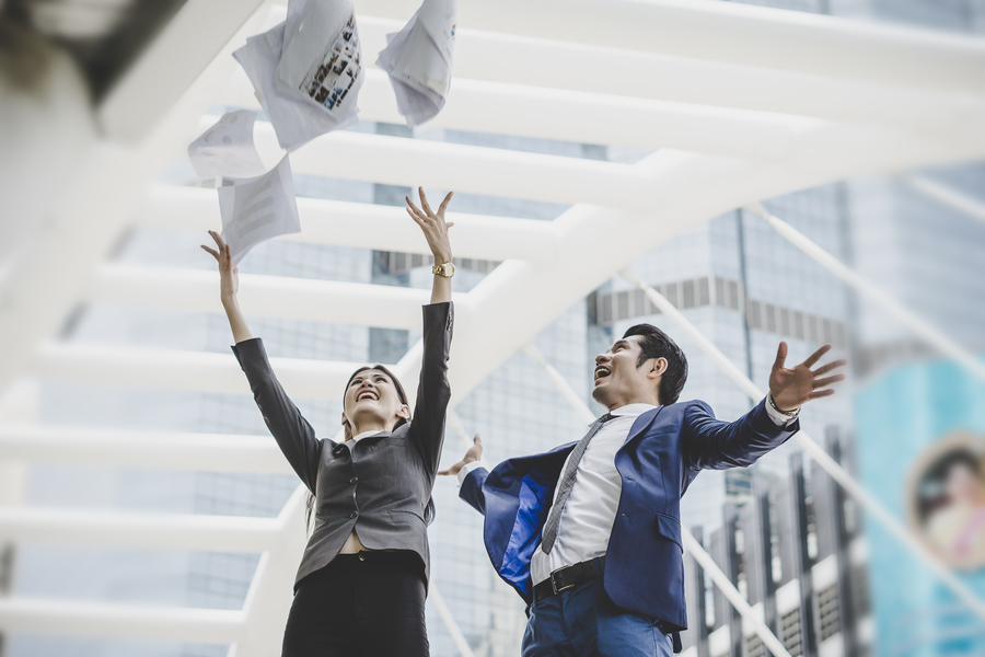 Business people are throwing up papers, while standing in front of office building. Business successfully concept.